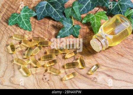 Capsule oblunghe gelatinose trasparenti di olio di pesce sono state sparse sullo sfondo di legno. Acidi grassi polinsaturi Omega-3-essenziali. Lasciare verde Foto Stock