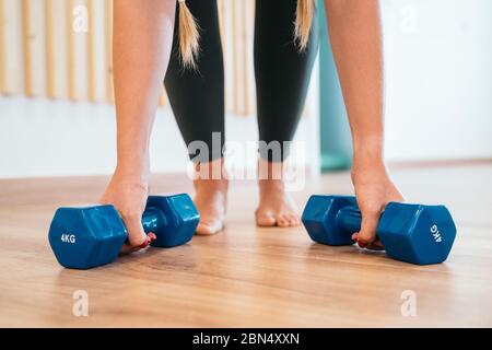 Primo piano di una giovane donna sportiva facendo esercizi push-up con manubri su pavimento in legno. Modello fitness che fa un allenamento intenso in palestra. Foto Stock