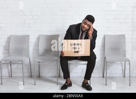 Uomo africano americano in tuta aziendale che tiene il segno CERCANDO LAVORO mentre attende l'intervista in ufficio. Spazio di copia Foto Stock