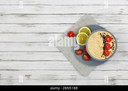 hummus composto da ceci in ciotole. su sfondo bianco decorato con pomodori, limone e tessuto. spazio copia. piatto Foto Stock