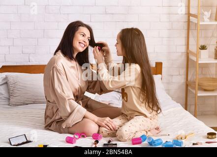 Madre figlia giorno dei capelli. Ragazza teen che mette i curlers sulla mamma in camera da letto Foto Stock