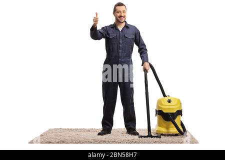Ritratto a tutta lunghezza di un janitor in uniforme con un aspirapolvere in piedi su un tappeto con pollici isolati su sfondo bianco Foto Stock