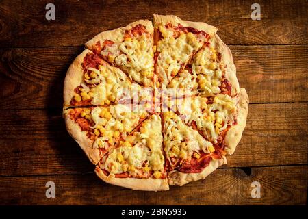la pizza cotta in casa viene tagliata a pezzi e giace su un tavolo di legno Foto Stock