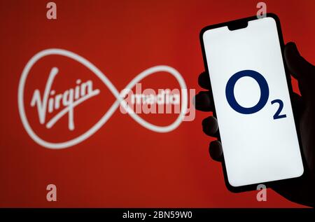 Stone / Regno Unito - Maggio 12 2020: O2 Telefono logo sullo schermo dello smartphone tenere in mano e Virgin Media logo su sfondo sfocato. Concetto per VI Foto Stock