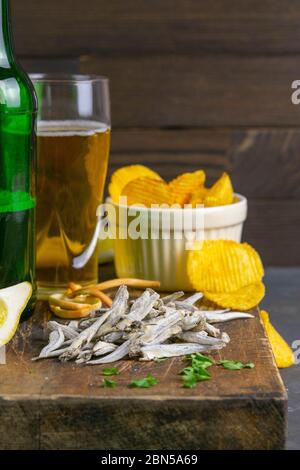 Acciughe salate secche con patatine di birra, limone e patate su asse di legno scuro. Snack a base di pesce con birra. Primo piano Foto Stock