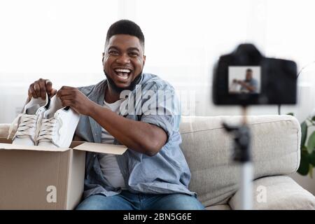 Joyful Black Man Blogger registrazione Unboxing Video di New Pair of Shoes Foto Stock