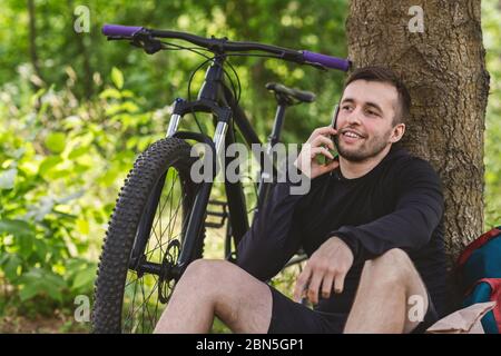 Primo piano di giovane ragazzo che parla per telefono sotto l'albero Foto Stock
