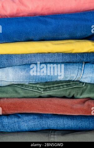 Pile di jeans e pantaloni ripiegati con precisione in colori vivaci. Sfondo astratto. Foto Stock