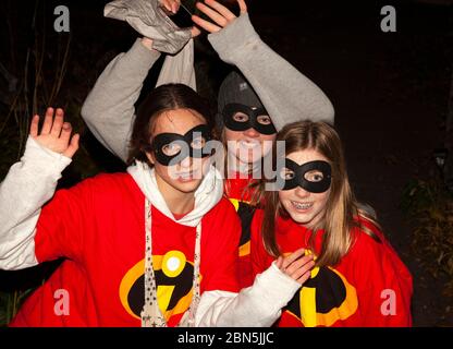 Ragazze teen che portano costumi Incredibles che hanno divertimento su Halloween fuori trucco e trattando. St Paul Minnesota, Minnesota, USA Foto Stock