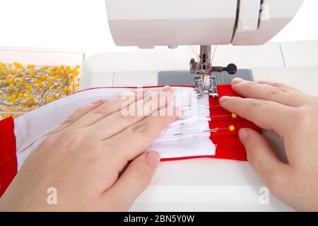 Primo piano delle mani fare maschera facciale stile chirurgico con tasca filtro di tessuti di cotone rosso brillante e bianco su una macchina da cucire bene usata. Isolato Foto Stock