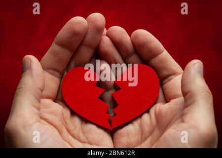 L'uomo tiene un cuore spezzato nelle sue mani. Crepa nel cuore rosso, rompendo il rapporto. Foto Stock