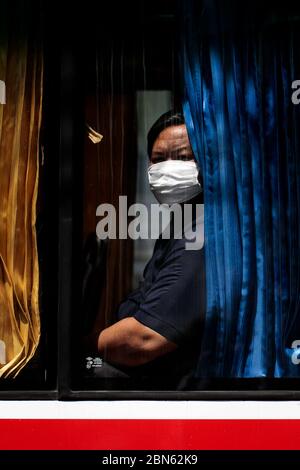 BANGKOK, THAILANDIA: Un passeggero indossa una maschera facciale e guarda fuori dalla finestra di un autobus pubblico durante l'alleggerimento delle restrizioni a Bangkok Thailandia il 12 maggio 2020 a seguito dell'epidemia di coronavirus COVID-19. Foto Stock