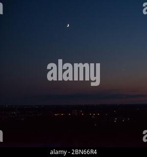 La luna sorge sopra le luci della città dopo il tramonto in foto log esposizione. Foto Stock