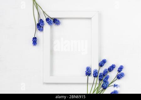 Cornice in legno bianco e bouquet di fiori blu su sfondo bianco. Vista dall'alto. Disposizione piatta. Foto Stock