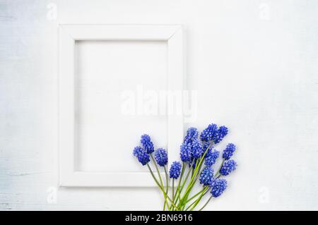 Cornice in legno bianco e bouquet di fiori blu su sfondo bianco. Vista dall'alto. Foto Stock