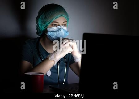 Donna caucasica infermiere medico in maschera chirurgica sembra stanco, esaurito di notte a causa di covid Foto Stock