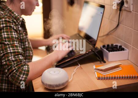 Diffusore di olio essenziale sul tavolo fumando mentre la donna d'affari usa il computer portatile durante covid-19. Foto Stock