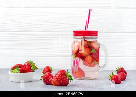 Acqua, cocktail, limonata o tè infusi con fragole. Bevanda fredda estiva ghiacciata con fragola, limone e foglia di menta su sfondo bianco di legno. Piatto Foto Stock