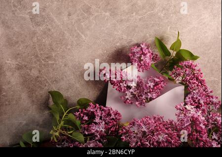 Lilacs viola che esce dalla busta bianca circondata da fiori. Foto orizzontale con spazio di copia a sinistra. Foto Stock