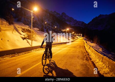 Ciclista in corse in strada di montagna a notte invernale Foto Stock