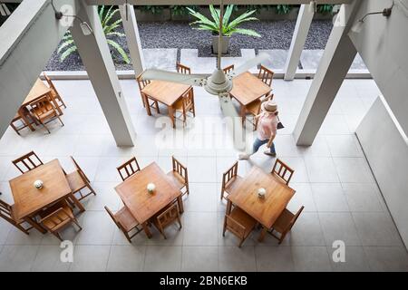 Donna in maglia rosa e hat è camminare vicino a tavola nel ristorante dell'hotel in Bangkok. Vista dall'alto. Foto Stock