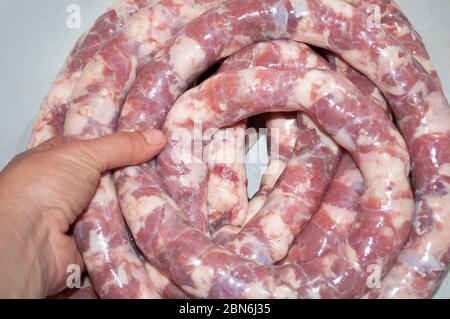 Fare la salsiccia fatta in casa. Il punto in cui la salsiccia cruda già farcito è arrotolata in un rotolo e pronta per la cottura. Potete vedere la mano che pu Foto Stock