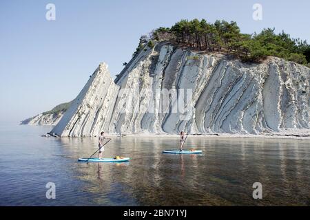 Giovane coppia che si accoppia a bordo di una SUP vicino alla bellissima formazione rocciosa. Foto Stock