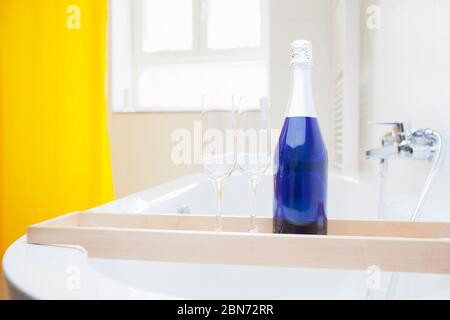 Bottiglia di champagne blu con due bicchieri da vasca in un bagno luminoso e pulito - concentratevi sulla bottiglia Foto Stock