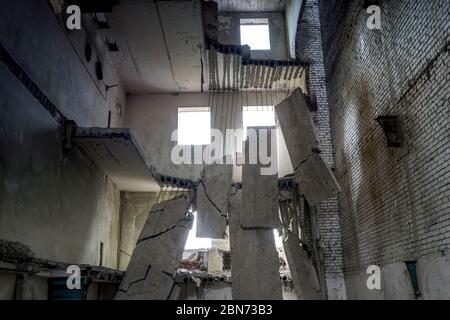 Edificio in cemento distrutto all'interno con un mucchio di detriti di costruzione in primo piano e grandi lastre di cemento appese sulla barra contro il muro posteriore Foto Stock