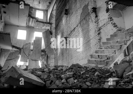 Immagine in bianco e nero. Edificio in cemento distrutto all'interno con un mucchio di detriti di costruzione in primo piano e grandi lastre di cemento appese a reba Foto Stock