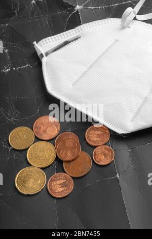 Maschera medica protettiva Kn95 e monete su sfondo astratto da vecchia carta nera sbriciolati. Un mucchio di centesimi di denaro con maschera ffp2. Il concetto di t Foto Stock