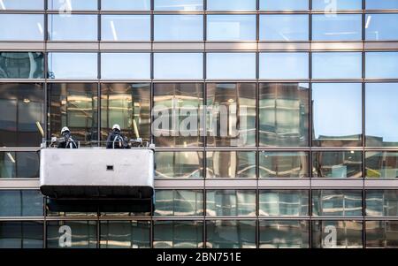 Pulitori per finestre che utilizzano un supporto sospeso per pulire l'esterno di un moderno blocco di uffici in vetro e acciaio. Foto Stock