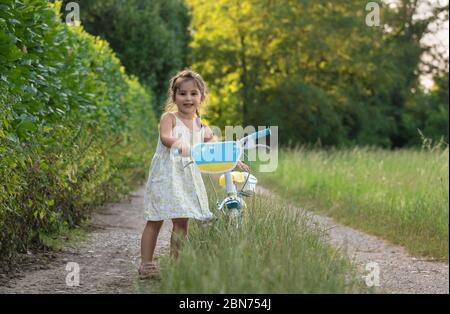 Una ragazza felice gioca con la sua bicicletta fuori su un sentiero nel mezzo della natura. Foto Stock