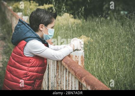 Coronavirus, triste e pensieroso bambino che indossa maschera medica all'aperto Foto Stock