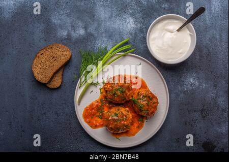 Polpette fatte in casa in salsa di pomodoro su un piatto bianco di ceramica con pane, cipolle e pomodori Foto Stock