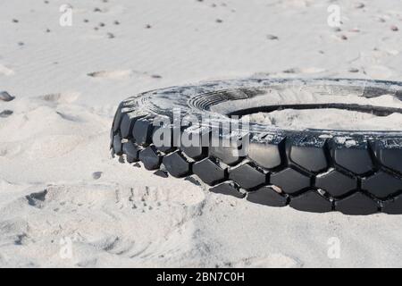 Grande pneumatico nero in gomma lasciato su una spiaggia sabbiosa, ambiente di inquinamento concetto Foto Stock