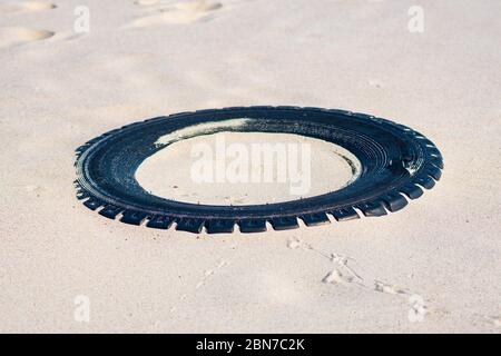 Grande pneumatico nero in gomma lasciato su una spiaggia sabbiosa, ambiente di inquinamento concetto Foto Stock