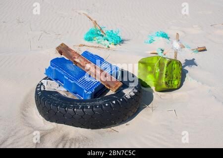 Grande pneumatico nero in gomma lasciato su una spiaggia sabbiosa con altri oggetti in plastica, ambiente di inquinamento concetto Foto Stock