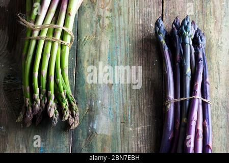 Due grappoli di spighe di asparagi verdi e viola biologiche coltivate in casa per cucinare cibo vegetariano sano da dieta su sfondo di legno, spazio copia Foto Stock