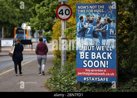 La gente cammina da un segno che dice 'ora non è il momento per gli hugs....ma saremo presto di nuovo!' Fuori dal McDiarmid Park, sede di St Johnstone. Foto Stock