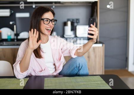 Donna sorridente seduta sul divano della cucina che parla da videocall datazione online guardando il telefono. Video blogger vlogger registrazione vlog a casa. Stile di vita vlo Foto Stock