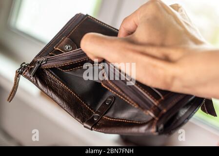 L'uomo sta tenendo una borsa vuota vuota del portafoglio di pelle marrone. Il concetto di crisi economica e fallimento delle imprese nel periodo post-pandemico Foto Stock