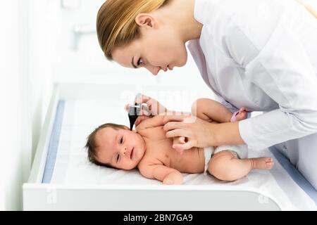 Pediatra esamina l'orecchio del bambino di 2 settimane in una nuova clinica pediatrica. Giovane medico che usa otoscopio (auriscopio) per controllare il canale uditivo e la membrana del timpano. Foto Stock