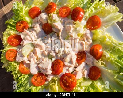 Primo piano di insalata estiva servita all'aperto con lattuga alla Frisée, pomodori ciliegini e salmone in maionese Foto Stock