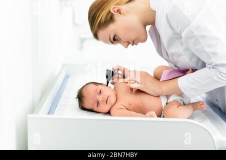 Pediatra esamina l'orecchio del bambino di 2 settimane in una nuova clinica pediatrica. Giovane medico che usa otoscopio (auriscopio) per controllare il canale uditivo e la membrana del timpano. Foto Stock