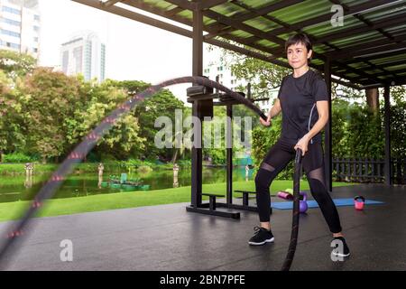 Donna asiatica con corda di battaglia corda di battaglia esercizio in palestra fitness. Foto Stock