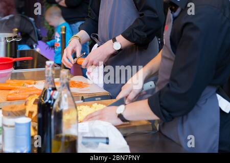 Uomini che tagliano e pelano le verdure (carote e patate) e preparano un pasto Foto Stock