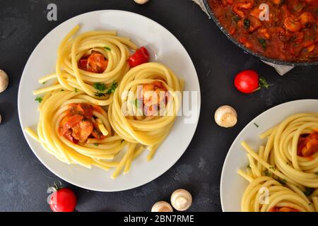 Pasta in un piatto bianco su fondo scuro. Spaghetti appetitosi con pomodori e funghi. Vista dall'alto. Foto Stock
