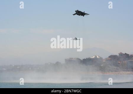 Serie 113 di 165 due McDonnell Douglas AV-8B Harrier II sorvolando e girando con la spiaggia e gli edifici dietro a. Forze armate giorno Spagna Foto Stock