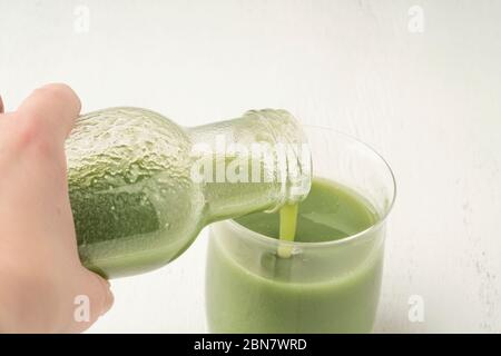 una mano che versa il frullato verde fresco del detox in un vetro Foto Stock